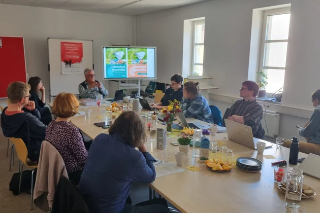 Ein Seminar-Raum mit mehreren Teilnehmenden, die auf einen großen Bildschirm schauen