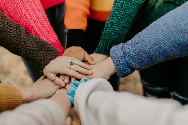 Übereinanderliegende Hände. Bunte Ärmel sichtbar. Sinnbild für Diversität