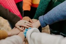 Übereinanderliegende Hände. Bunte Ärmel sichtbar. Sinnbild für Diversität